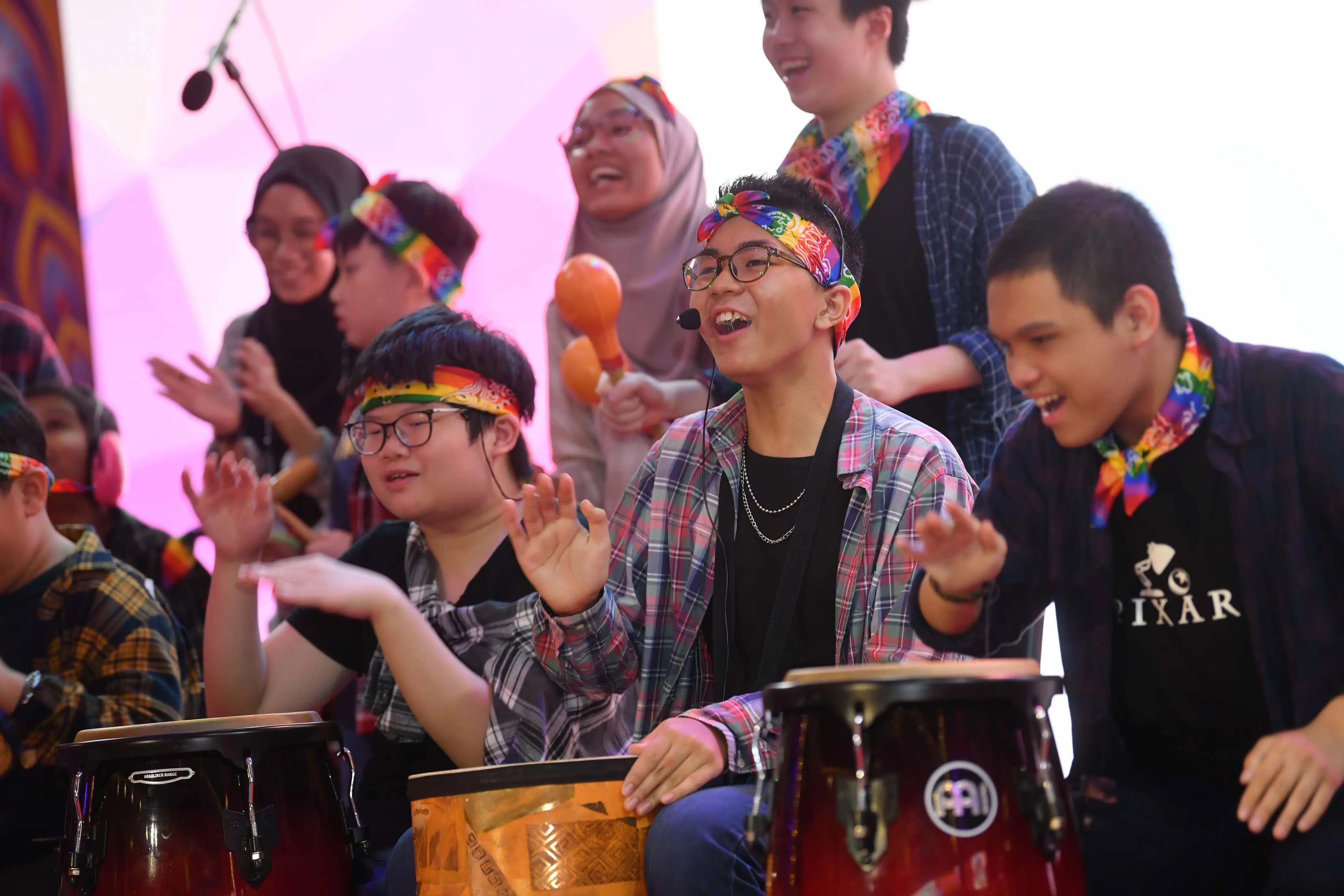 People wearing colourful headbands and scarves are playing various percussion instruments on a stage.